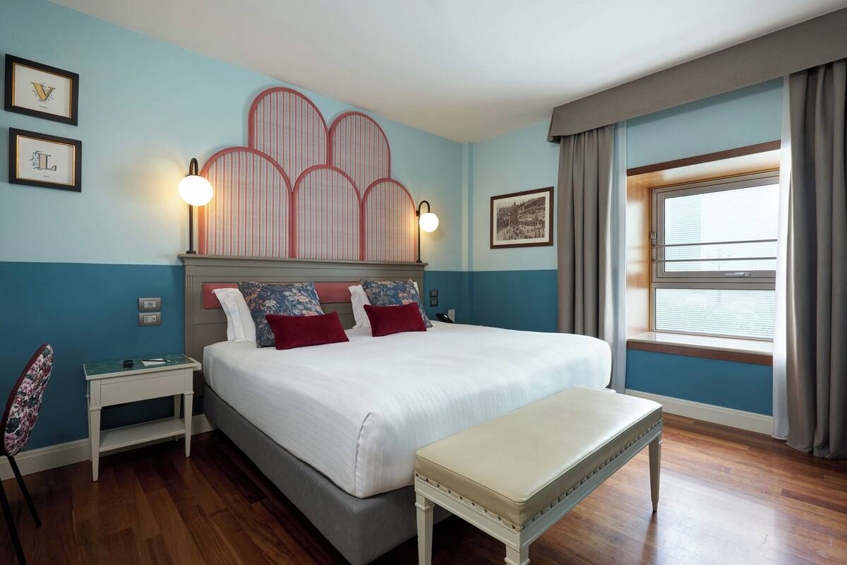A neatly arranged bedroom with a large bed, bedside tables, a bench, and a window with curtains.