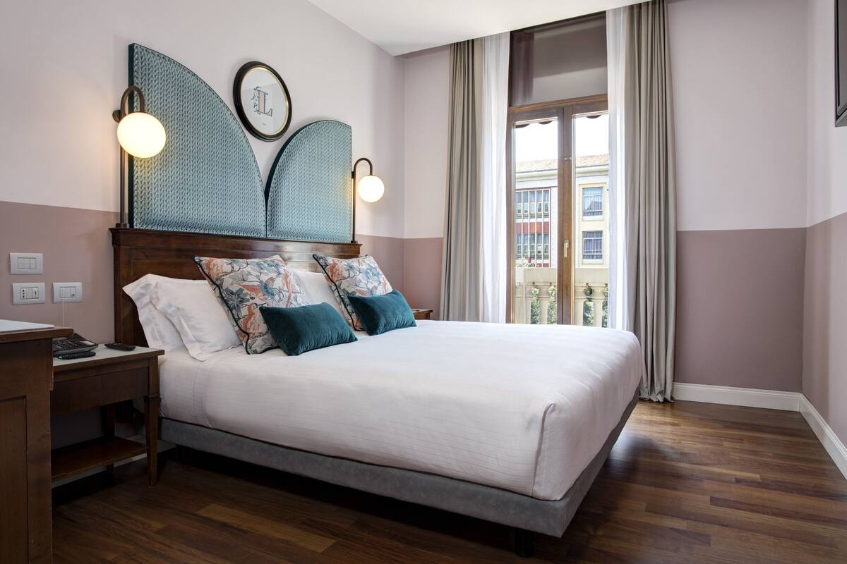 A neatly arranged bedroom with a large bed, a bedside table, and a view of the outside balcony.