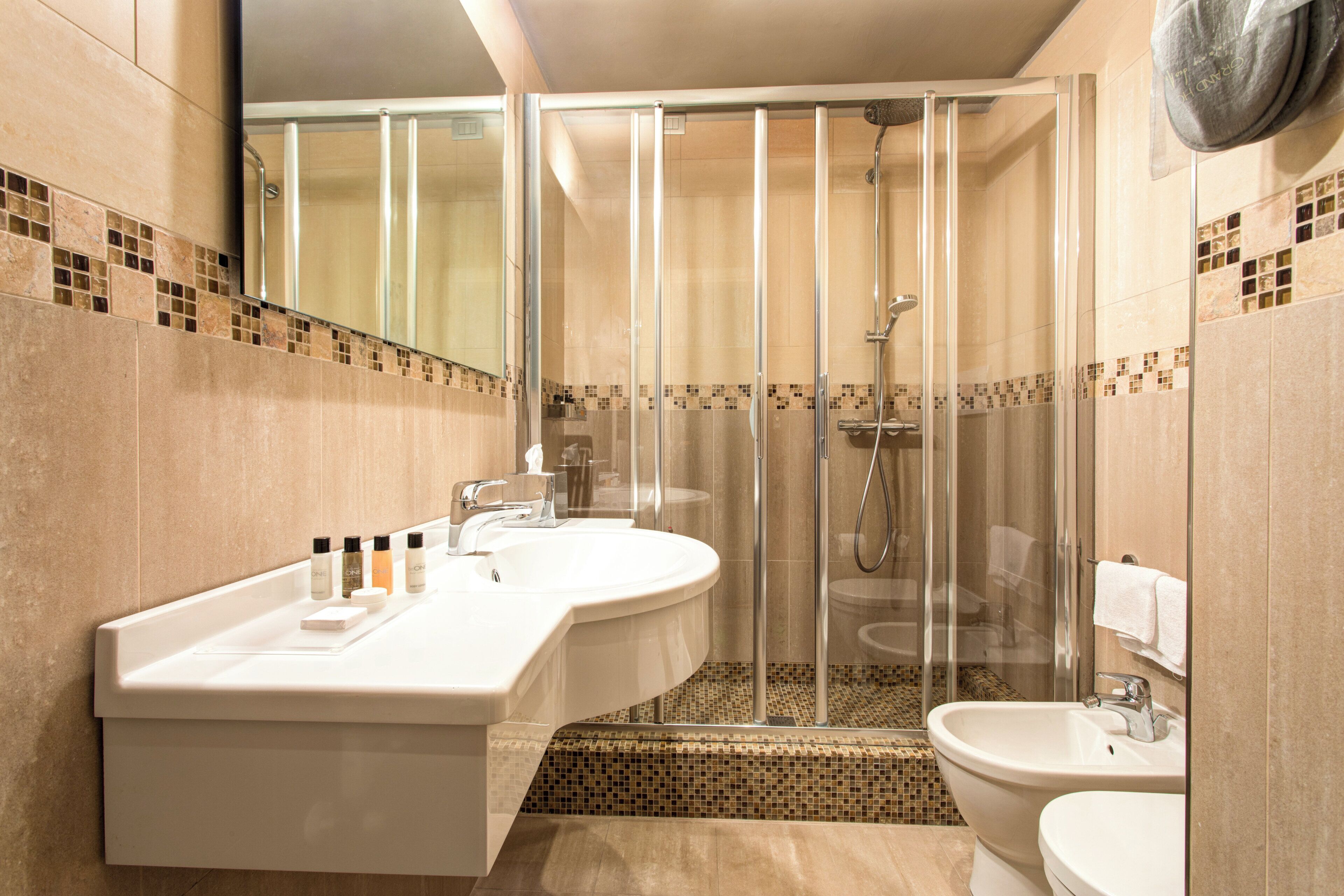A modern bathroom with a glass-enclosed shower, a large vanity with a mirror, and a bidet.