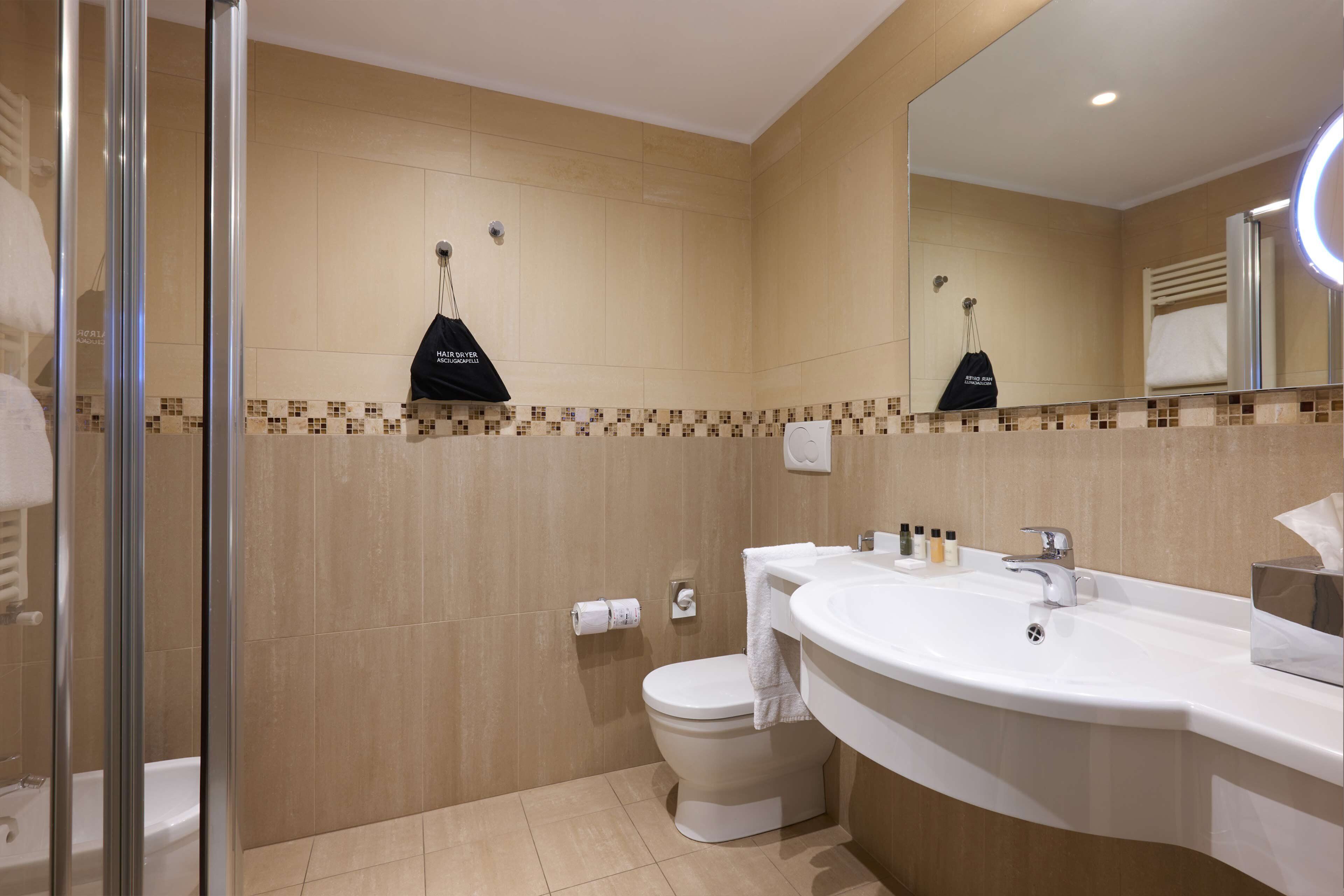 Un bany modern amb una dutxa de vidre, un vàter blanc i un lavabo amb un mirall gran.