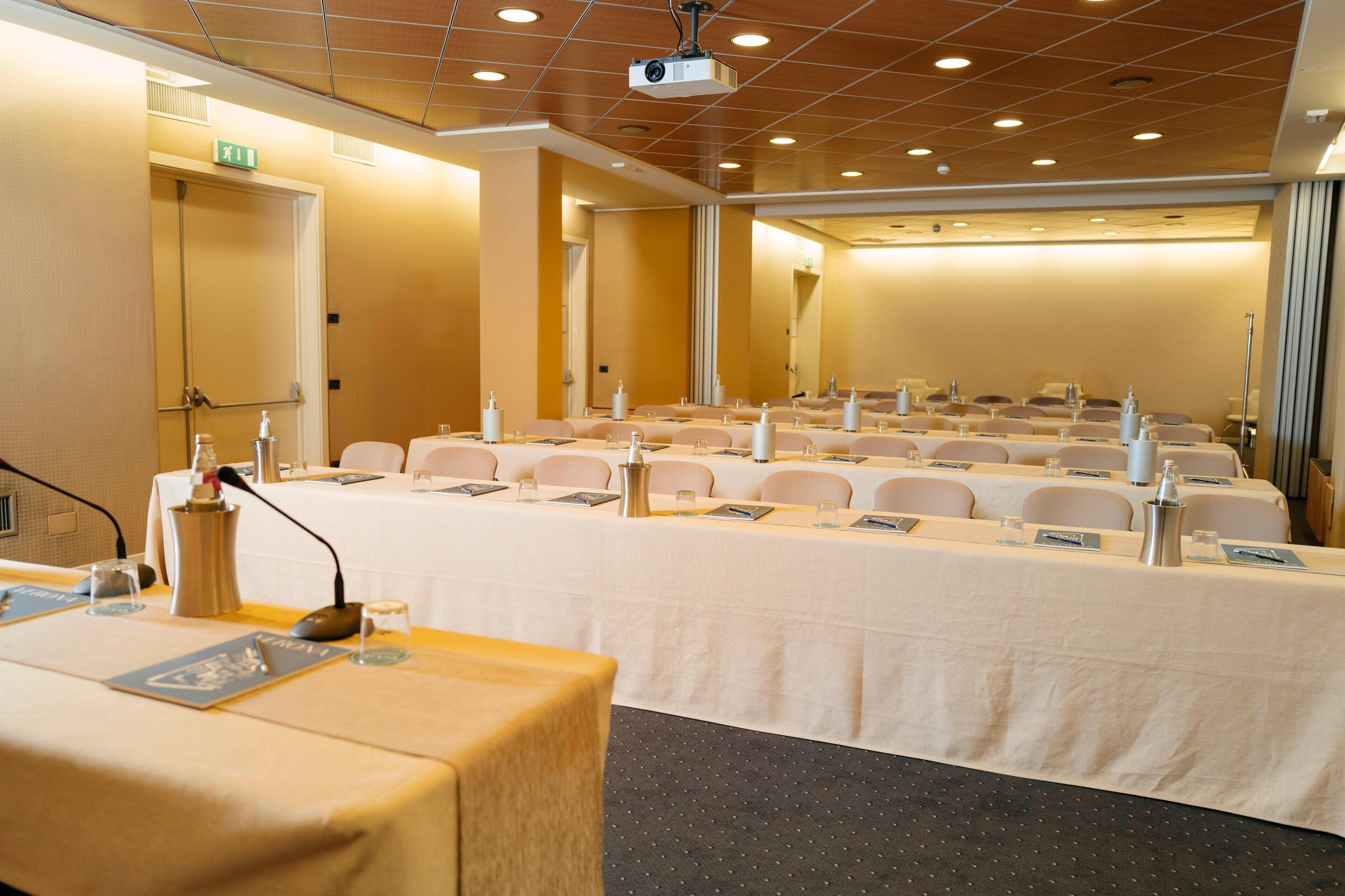 A conference room with rows of tables, chairs, and a podium with a microphone.