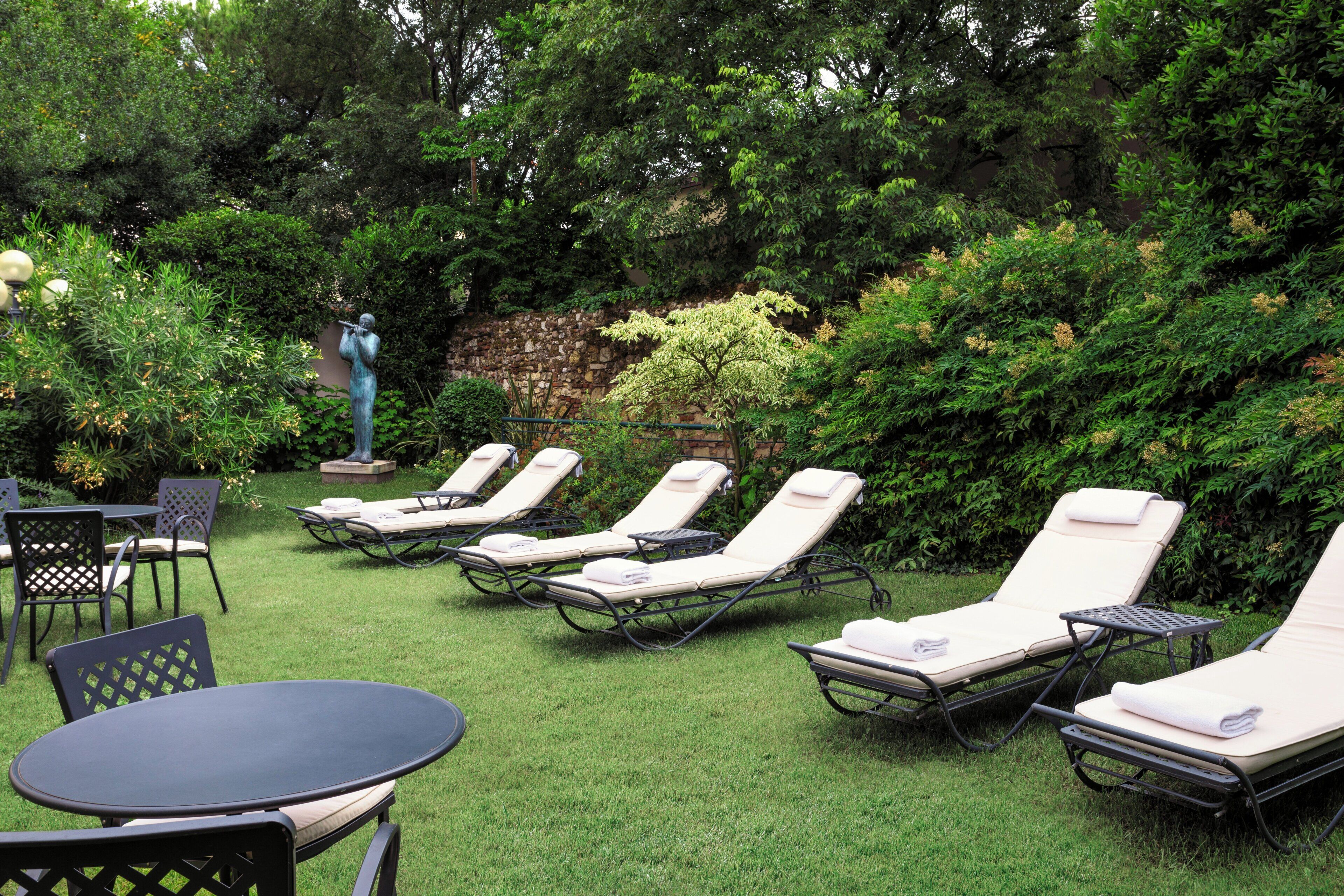 Un jardin doté de plusieurs chaises longues et d’une table, entouré d’une végétation luxuriante et d’un mur de pierre.