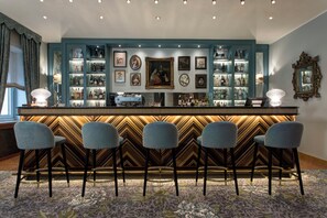 Una zona de bar con una barra de diseño en zigzag, taburetes y una colección de obras de arte enmarcadas en la pared.