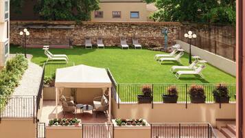 Una terraza en la azotea con césped, sillas de descanso, un área de estar cubierta y plantas en macetas.