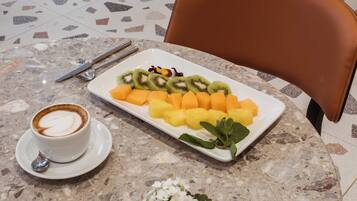 A marble table with a white plate of fruit, a cup of coffee, and a pair of cutlery.