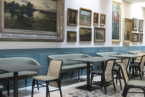 Un comedor con mesas y sillas, un cuadro grande en la pared, y una pared de acento azul.