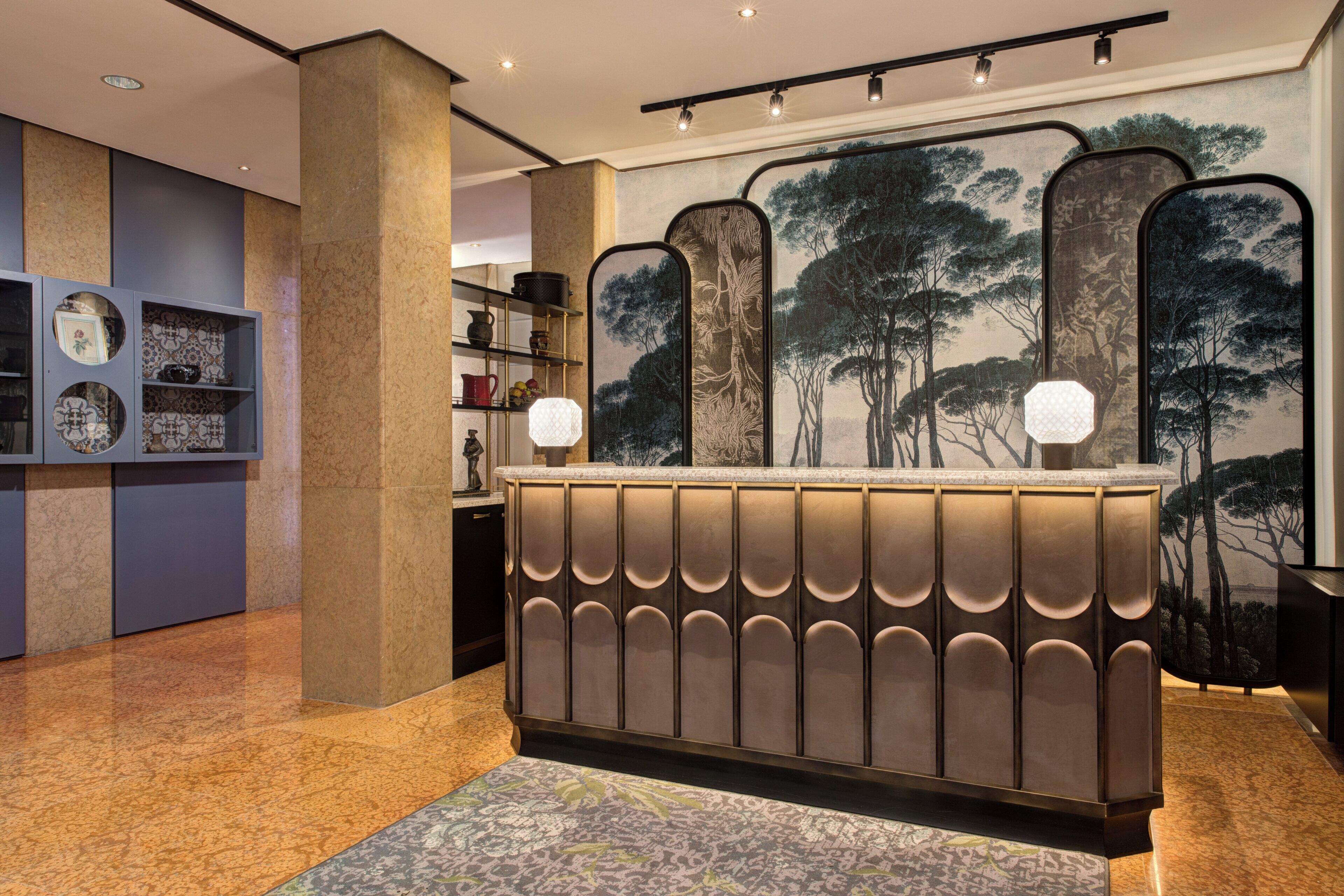 Un área de recepción con diseño moderno, que cuenta con un mostrador central y un respaldo con textura, además de dos lámparas fijadas a la pared.