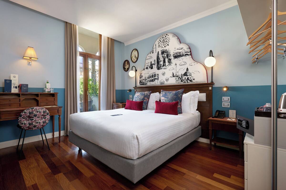 A hotel room with a large bed, wooden floor, desk, chair, bedside tables, and a decorative headboard.