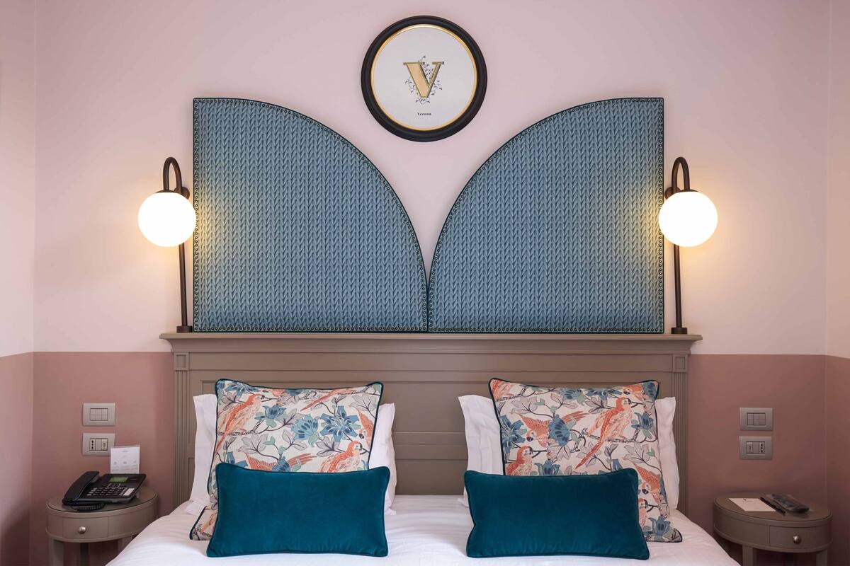 A hotel room with a large bed, two nightstands, a wall-mounted light fixture, and a decorative wall piece.