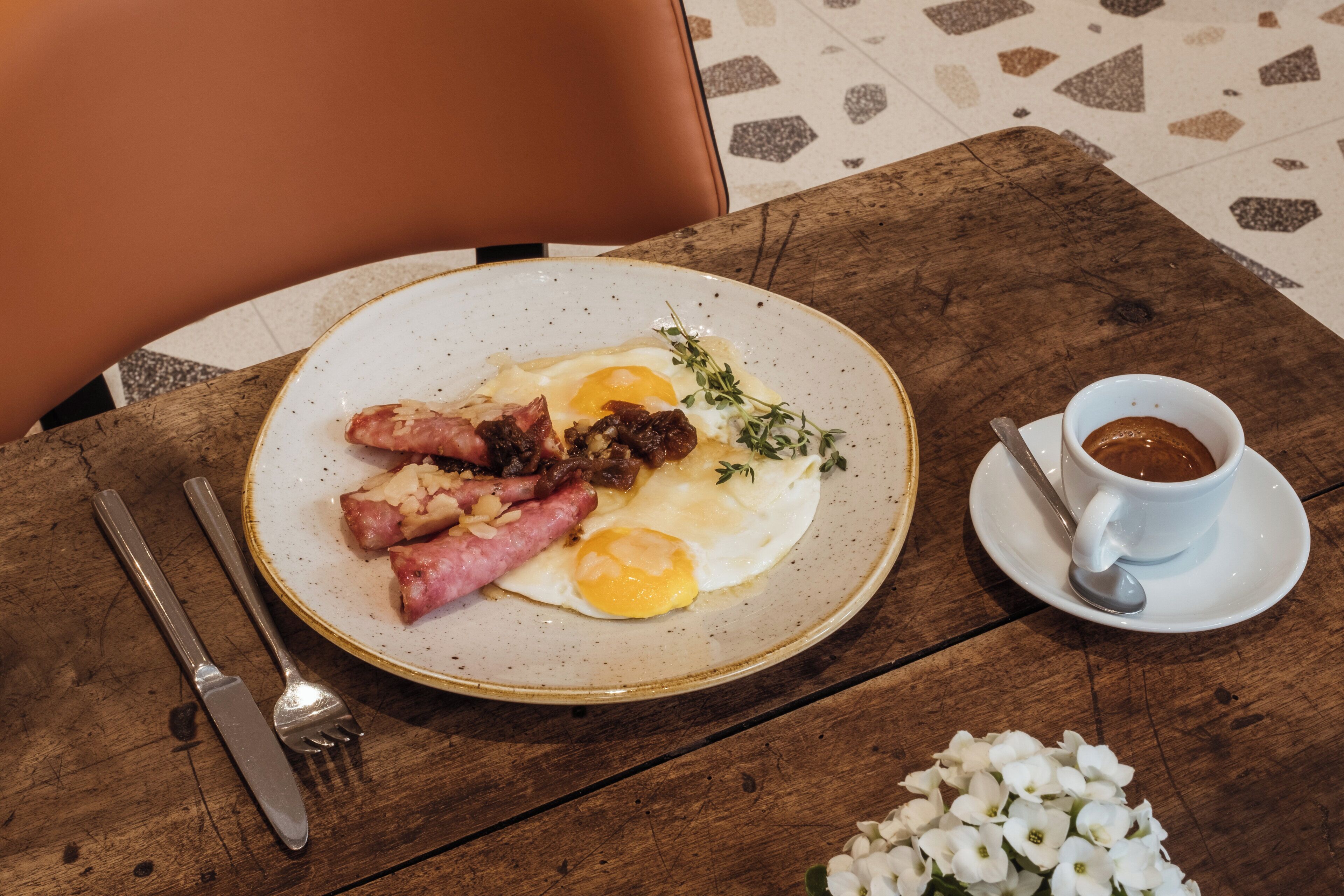 A breakfast plate with eggs, sausages, and a cup of coffee on a wooden table.