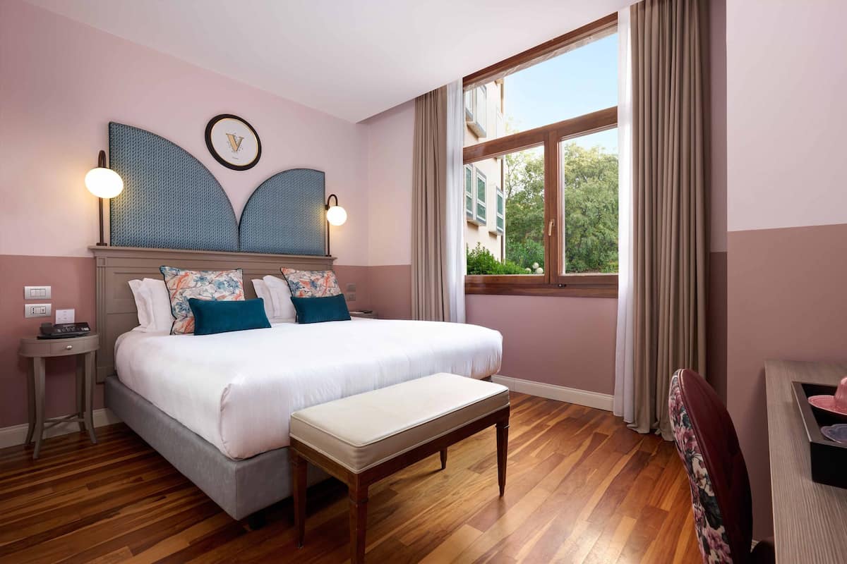 A neatly arranged bedroom with a large bed, bedside tables, a bench, and a view of greenery outside.
