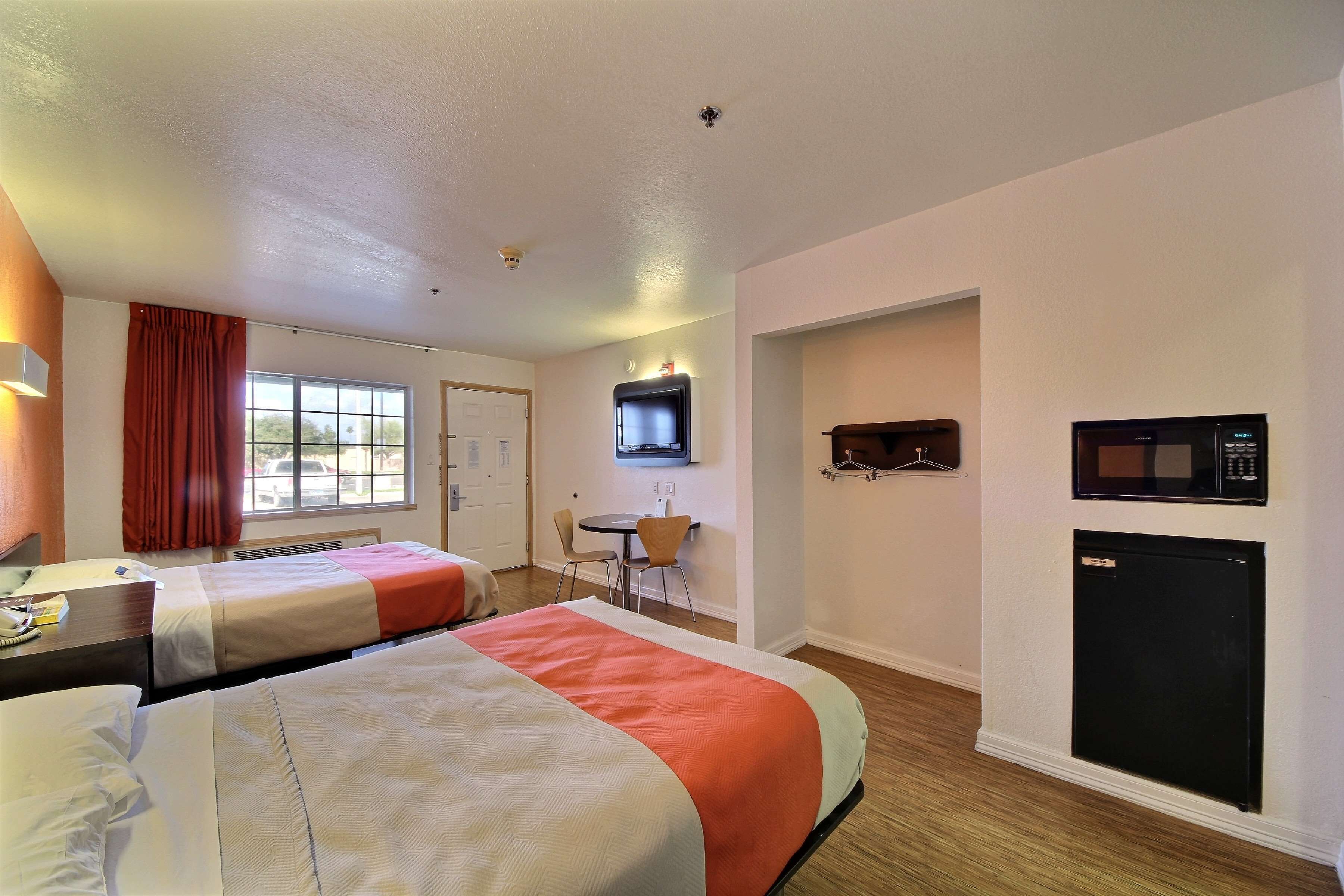 A hotel room with two beds, a desk with a telephone, a TV mounted on the wall, a microwave, and a refrigerator.