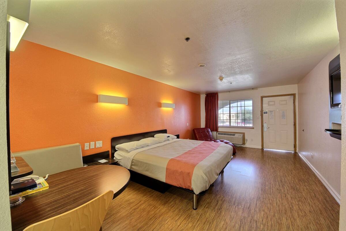 A hotel room with a bed, desk, and chair, a window with curtains, and a door.