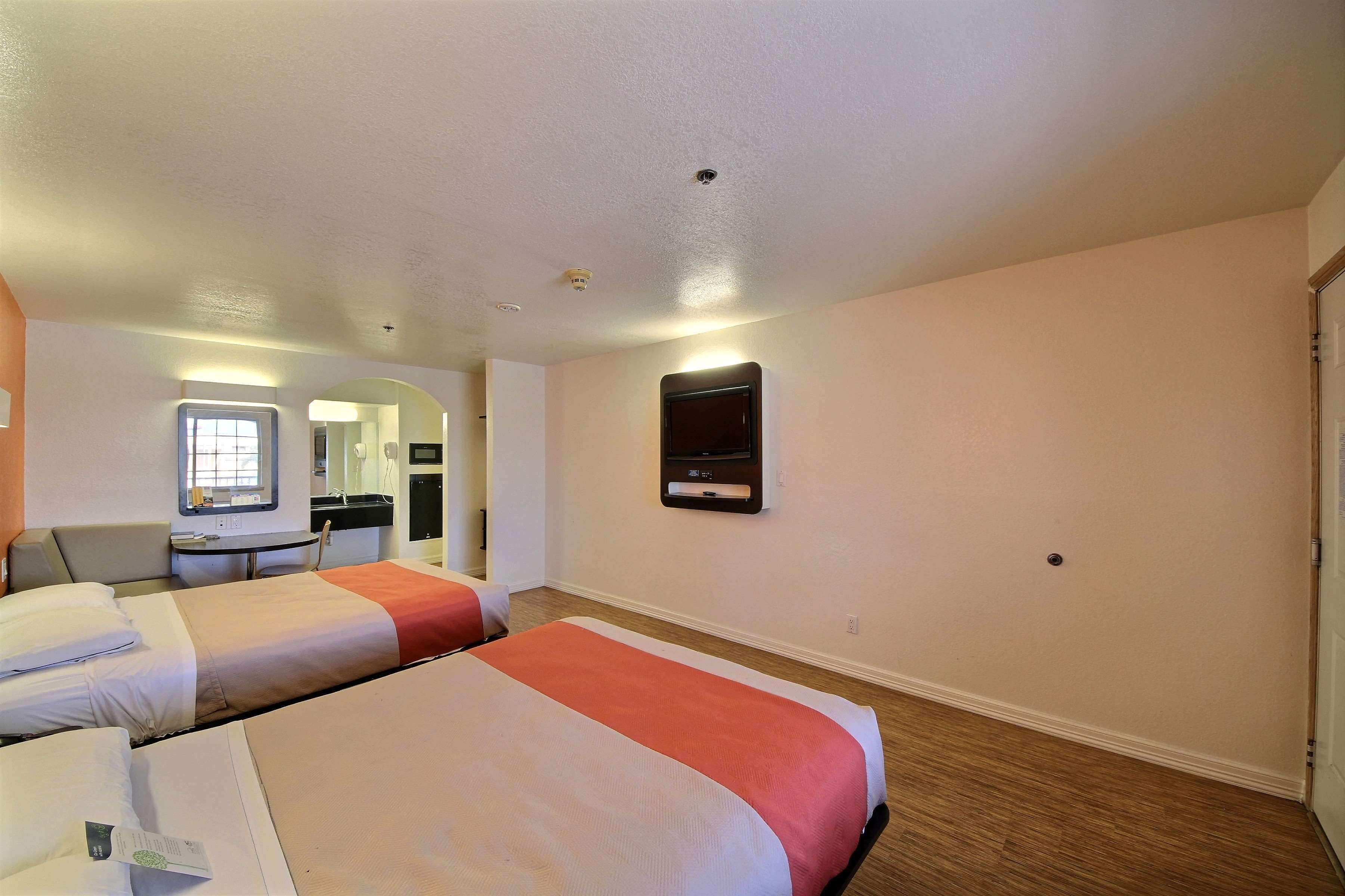 A hotel room with two beds, a desk, a chair, a TV, and a mirror.