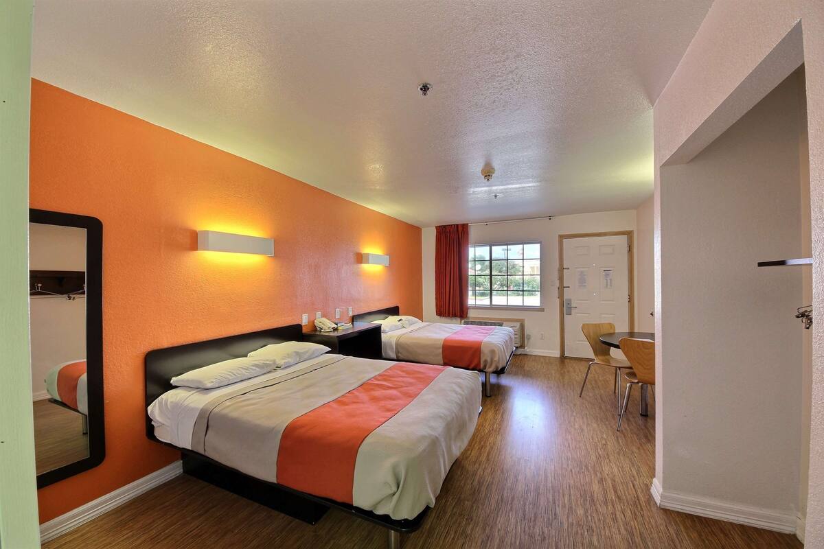 A hotel room with two beds, a large mirror, a desk, and a window.
