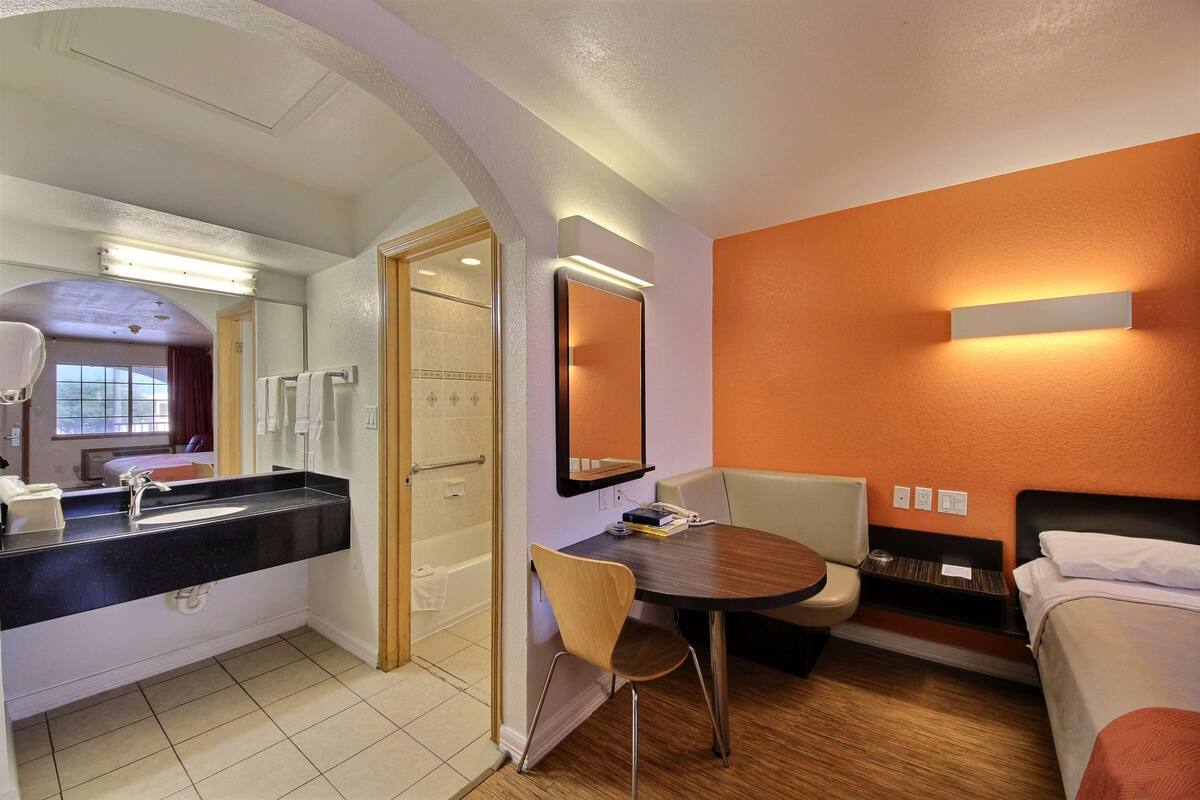 A hotel room with a bathroom, a dining table, and a bed.