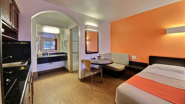 Une chambre d’hôtel comprenant un lit, un bureau, une chaise, une petite table, un miroir et une salle de bain visible à travers une arche.