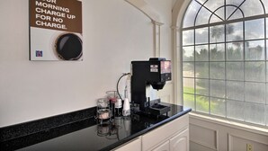 Une machine à café posée sur un comptoir noir, avec une pancarte au-dessus indiquant : « VOTRE DOSE DE CAFÉ MATINALE, OFFERTE ».