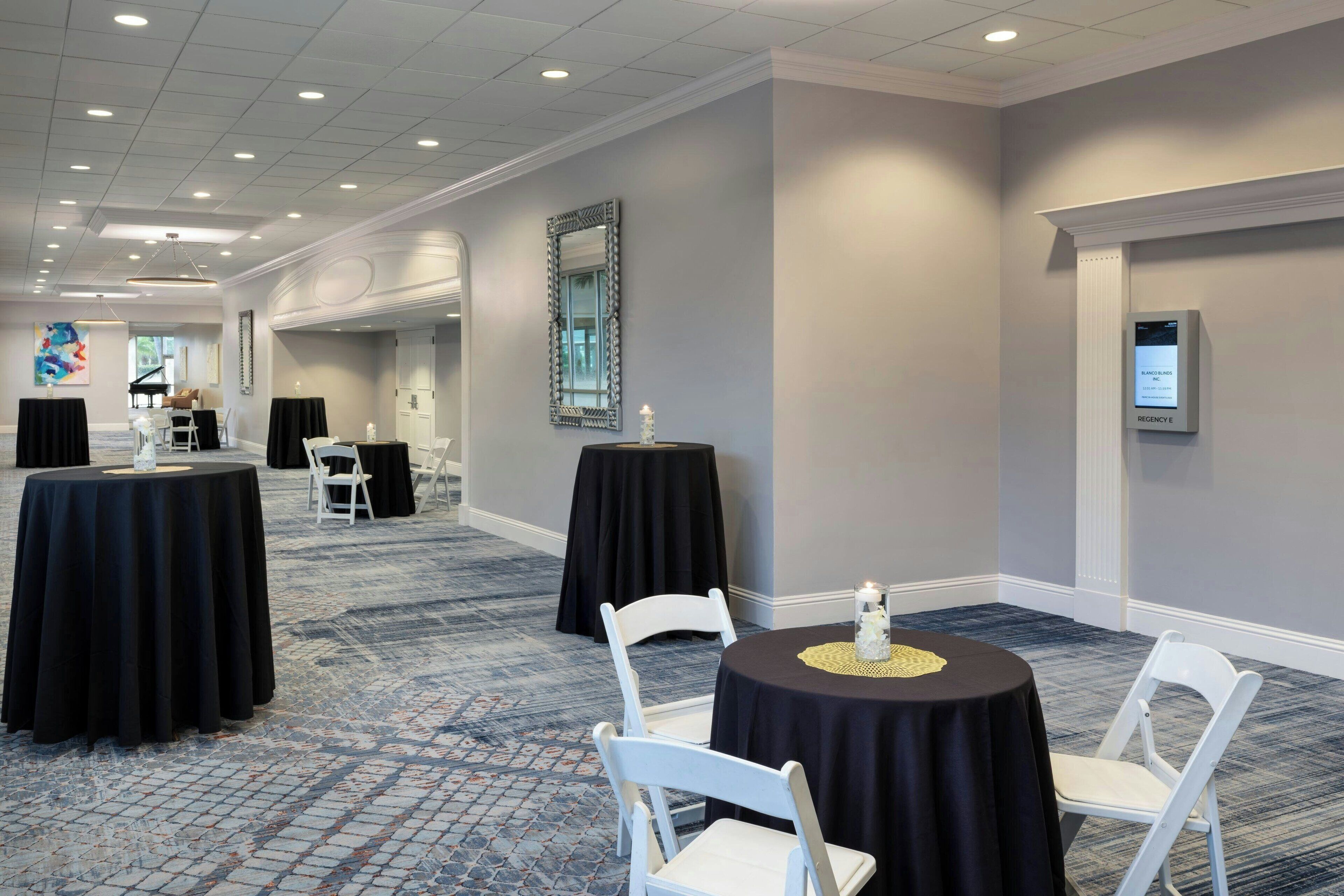 A conference room with round tables, white chairs, and a carpeted floor.