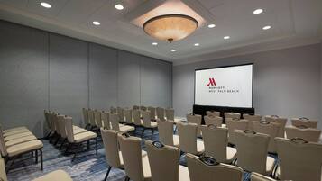 A conference room with rows of beige chairs, a large screen, and a carpeted floor.