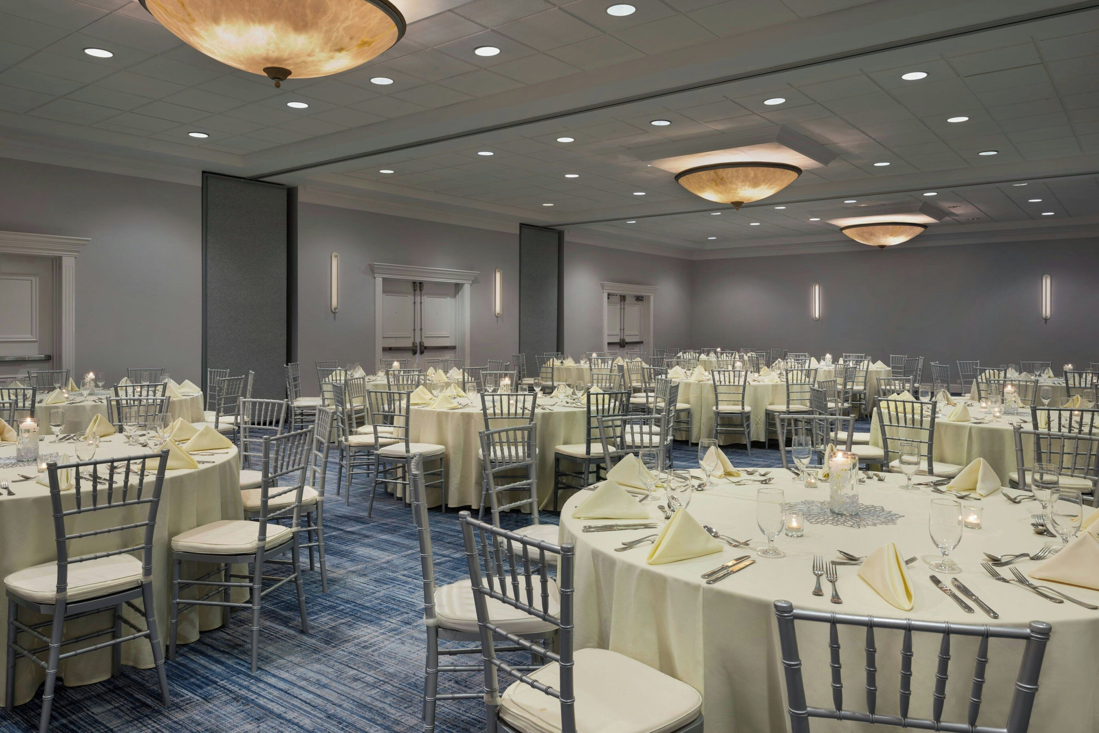 Une salle de banquet avec des tables rondes dressées pour le repas, équipées de chaises et de couverts.