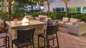 Une terrasse extérieure avec une table de feu en pierre, des fauteuils en osier et un canapé.
