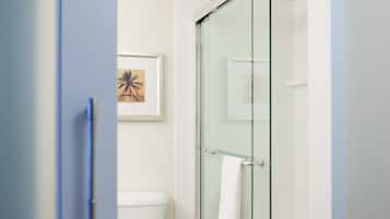 Une salle de bain moderne avec une douche à parois de verre, une œuvre d’art encadrée accrochée au mur et une serviette blanche suspendue à la poignée de la porte de la douche.