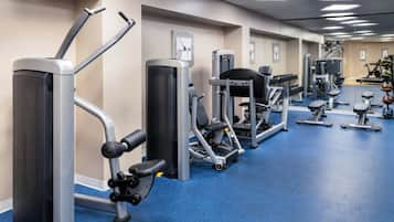 Ett gym med olika träningsmaskiner, ett blått golv och speglar på väggarna.