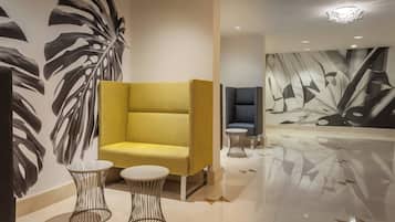 A modern lobby with a yellow sofa, two wireframe tables, and a large abstract mural on the wall.