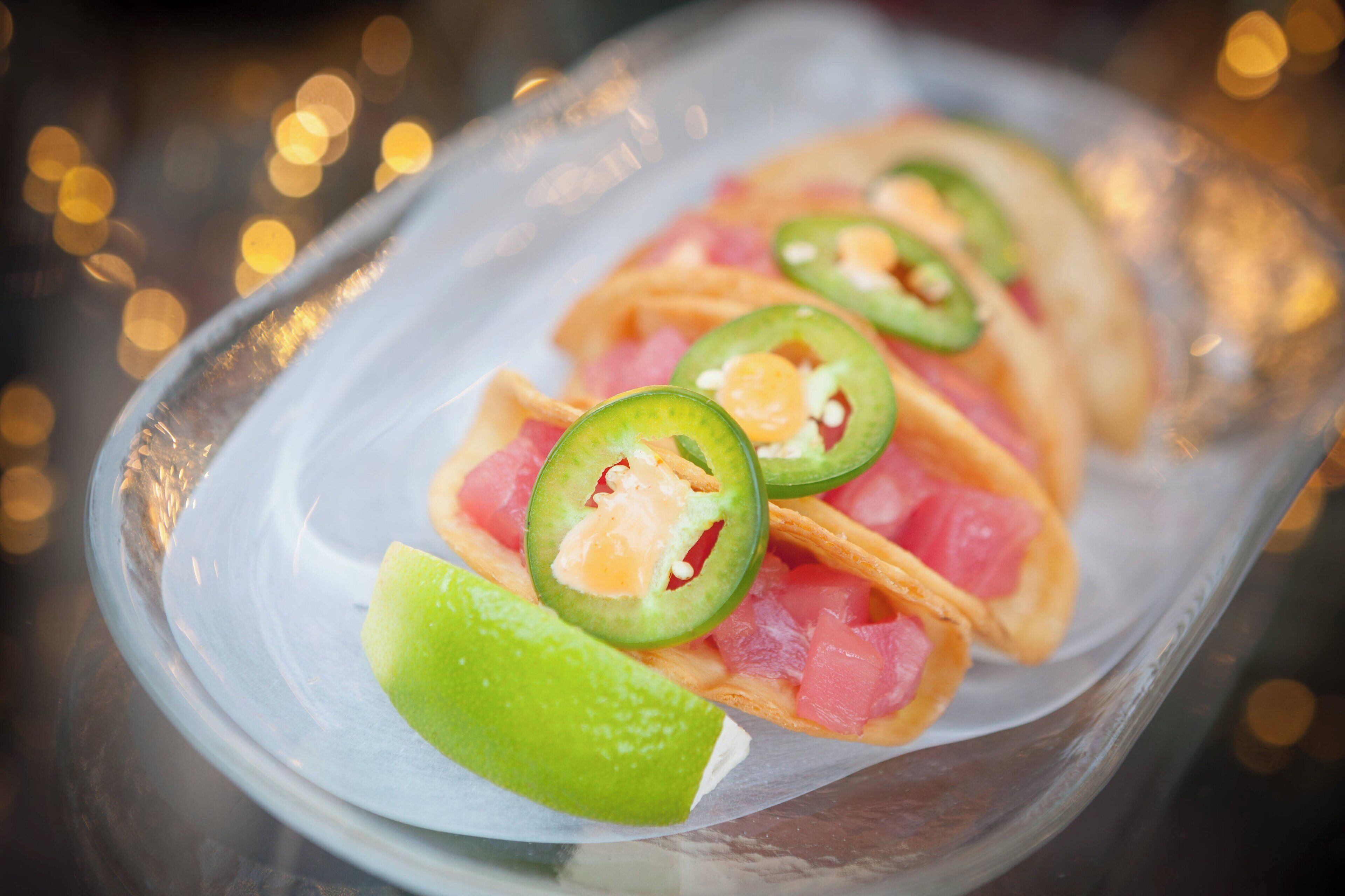 Un piatto di vetro con tacos, jalapeños e spicchi di lime.