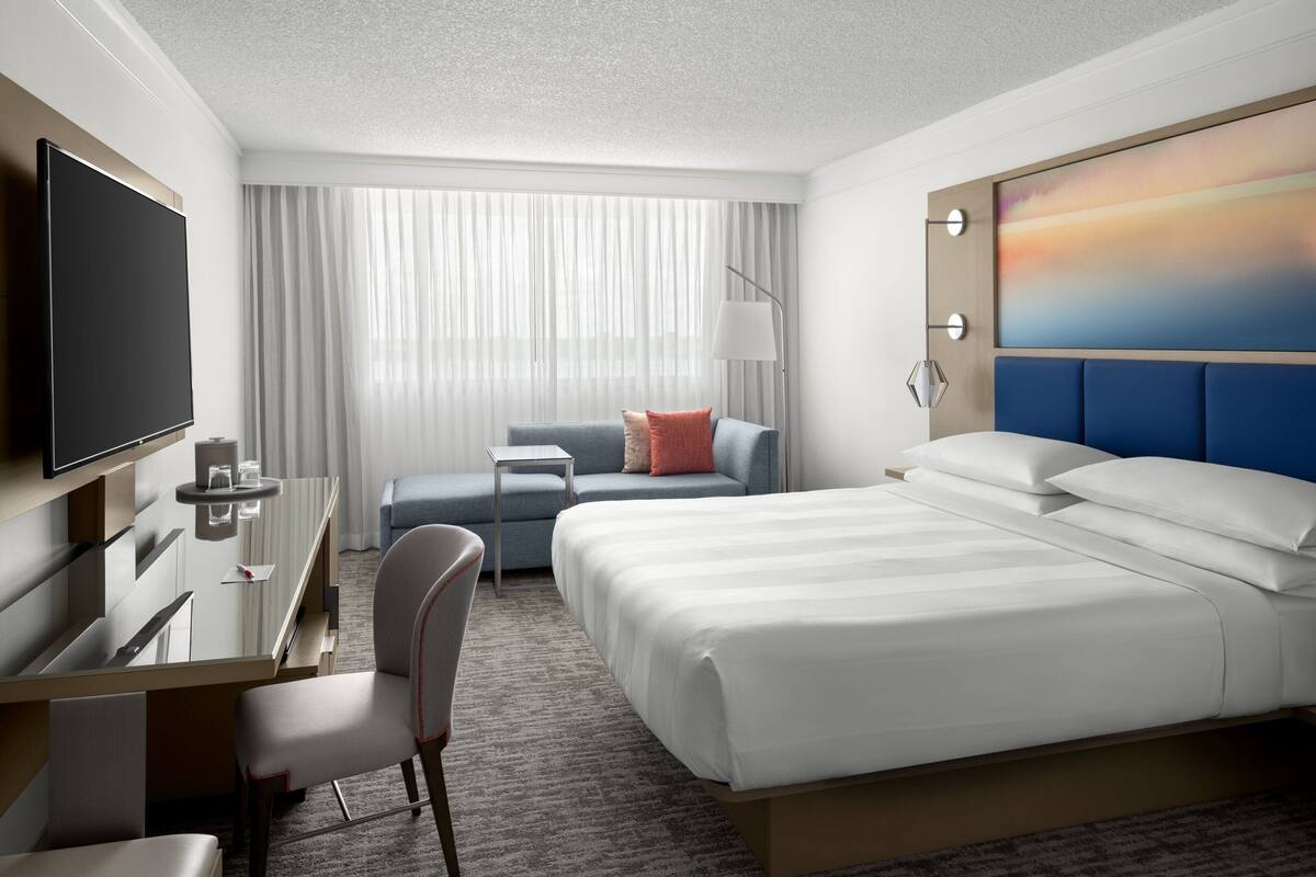 Een hotelkamer met een groot bed, een bureau met stoel, een televisie, een bank en een schilderij aan de muur.