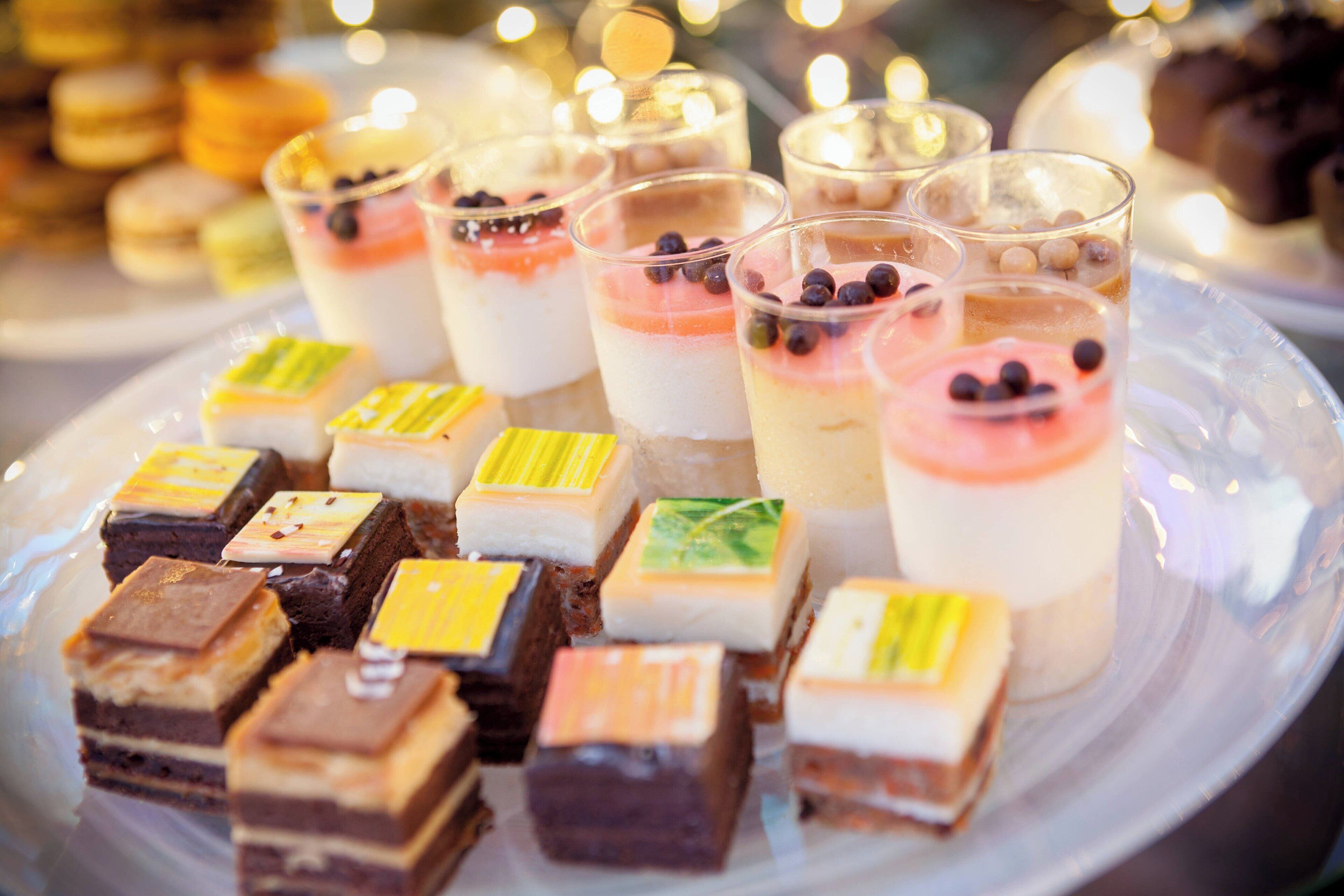 A variety of desserts on a plate, including layered parfaits and square-shaped desserts with different toppings.