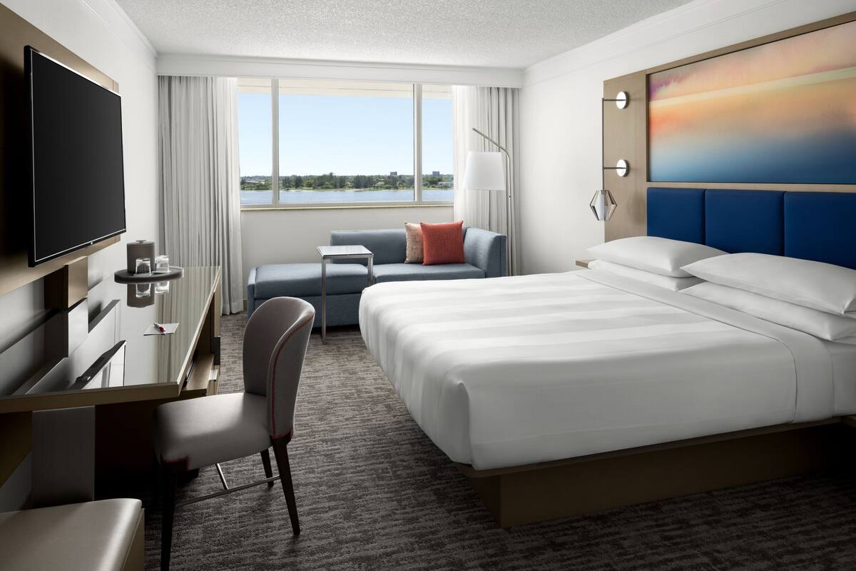 Een hotelkamer met een bed, een bureau met stoel, een televisie en uitzicht op een meer.