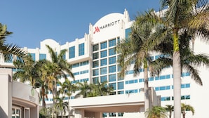 Un hotel Marriott con fachada blanca moderna, varios pisos y una entrada destacada con palmeras y un paseo techado.