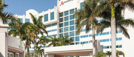 A Marriott hotel with a modern white facade, multiple floors, and a prominent entrance with palm trees and a covered walkway.