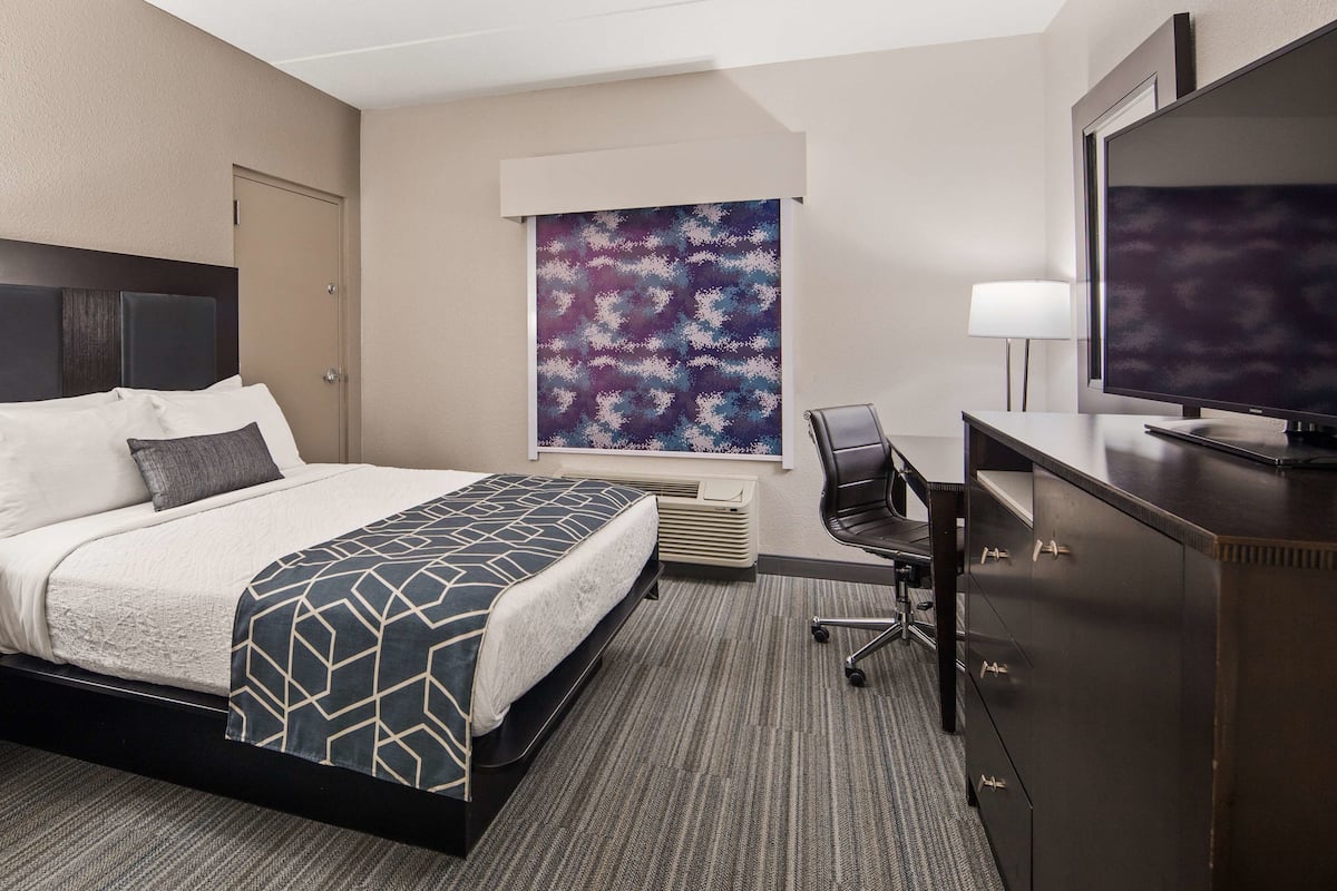 A hotel room with a bed, a desk with a chair, a television, and a large window.