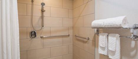 A shower area with a handheld showerhead, a wall-mounted control, and a towel rack with two towels.