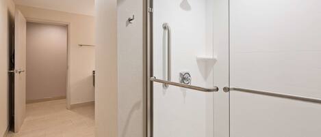 Un baño moderno con cabina de ducha de vidrio, pasamanos y pared revestida de azulejos blancos.