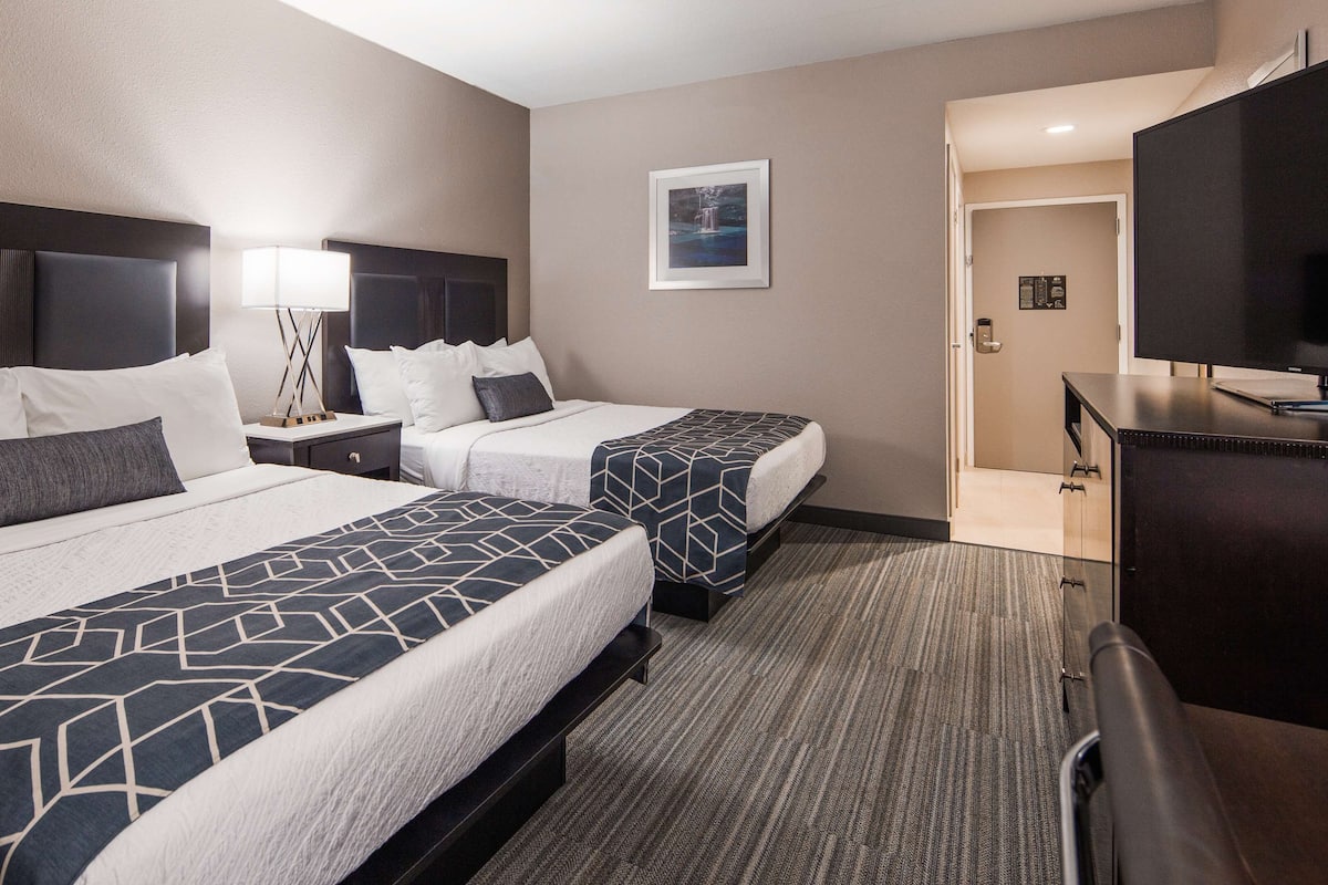 A hotel room with two beds, a desk, a TV, and a framed picture on the wall.
