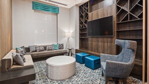 A modern living room with a sofa, ottoman, and a unique chair, a TV mounted on a wooden wall, and a patterned floor.