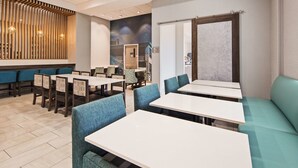 A restaurant with a modern interior, featuring wooden panel walls, blue upholstered booths, and white tables.