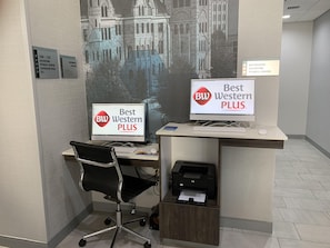 Two computer workstations with 'Best Western PLUS' branding, a black office chair, a printer, and a wall-mounted sign indicating elevators and a fitness center. - Best Western Plus Wilkes Barre-Scranton Airport Hotel (Avoca)