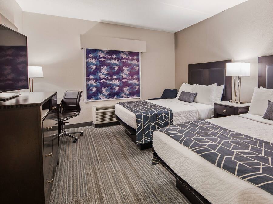 A hotel room with two beds, a desk, a chair, a large abstract painting, and a window.