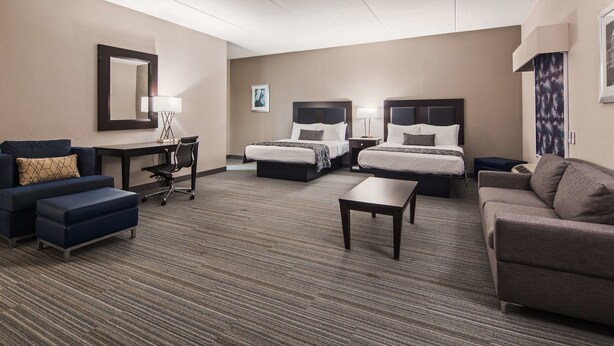 A hotel room with two beds, a desk, a chair, a sofa, and a carpeted floor.