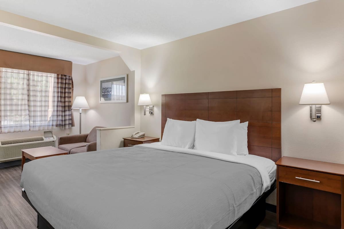 A hotel room with a large bed, a desk, a chair, a lamp, and a window with curtains.