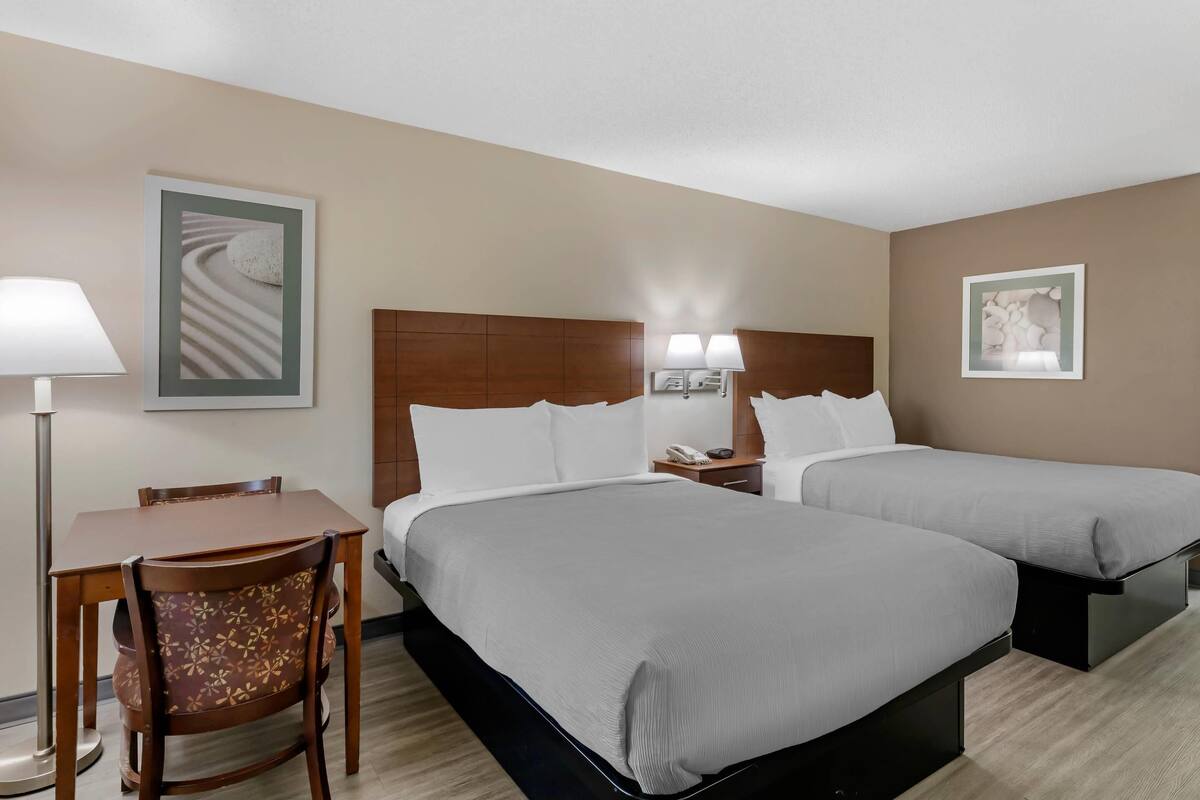 A hotel room with two beds, a desk, and a chair.