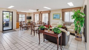 A spacious living area with a dining table, chairs, a sofa, and a TV. There are potted plants and a large window with curtains. - Quality Inn & Suites Stockbridge Atlanta South I-75 (Stockbridge)