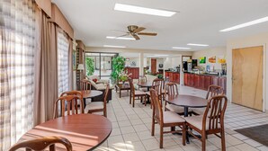 A spacious dining area with multiple round tables and wooden chairs, a ceiling fan, and a kitchen in the background. - Quality Inn & Suites Stockbridge Atlanta South I-75 (Stockbridge)