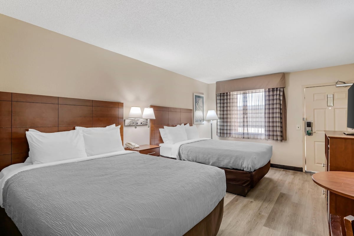 A hotel room with two beds, a wooden headboard, bedside lamps, a desk, and a television.