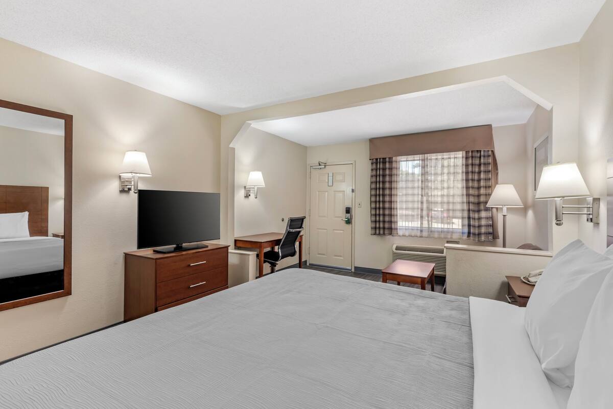 A hotel room with a large bed, a desk, a chair, a television, and a window with curtains.